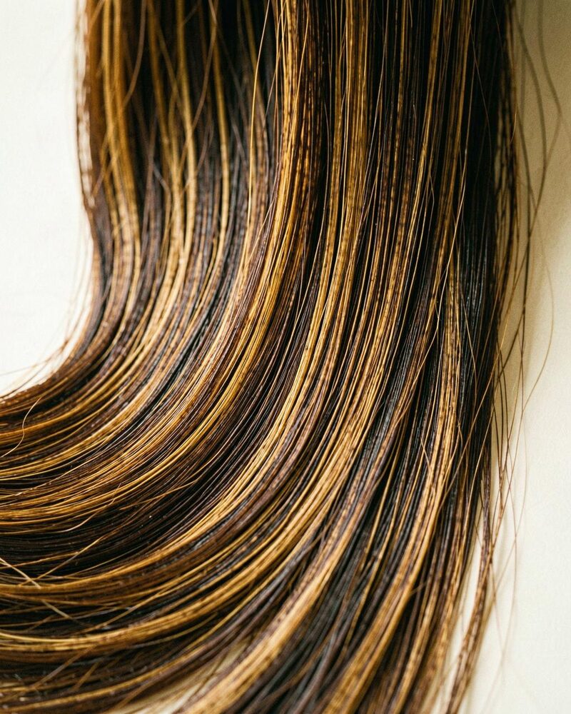 Long brunette extension hair with caramel highlights falling in one smooth, glossy sheet
