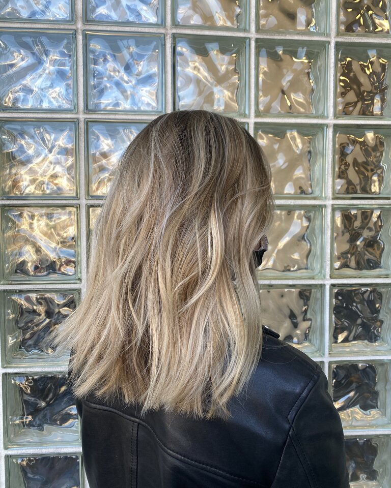 Shoulder-length wavy blonde bob, photographed from behind against a frosted glass-block wall