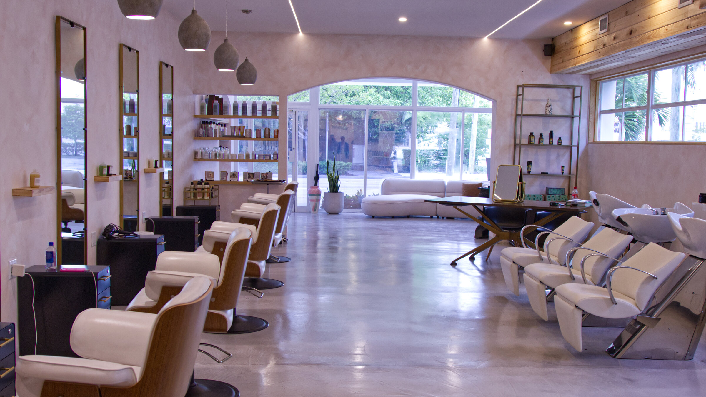 Interior of Red Market & Martial Vivot French hair salon in West Palm Beach — vintage wood styling stations, brass chandeliers, and an arched window onto S Dixie Hwy