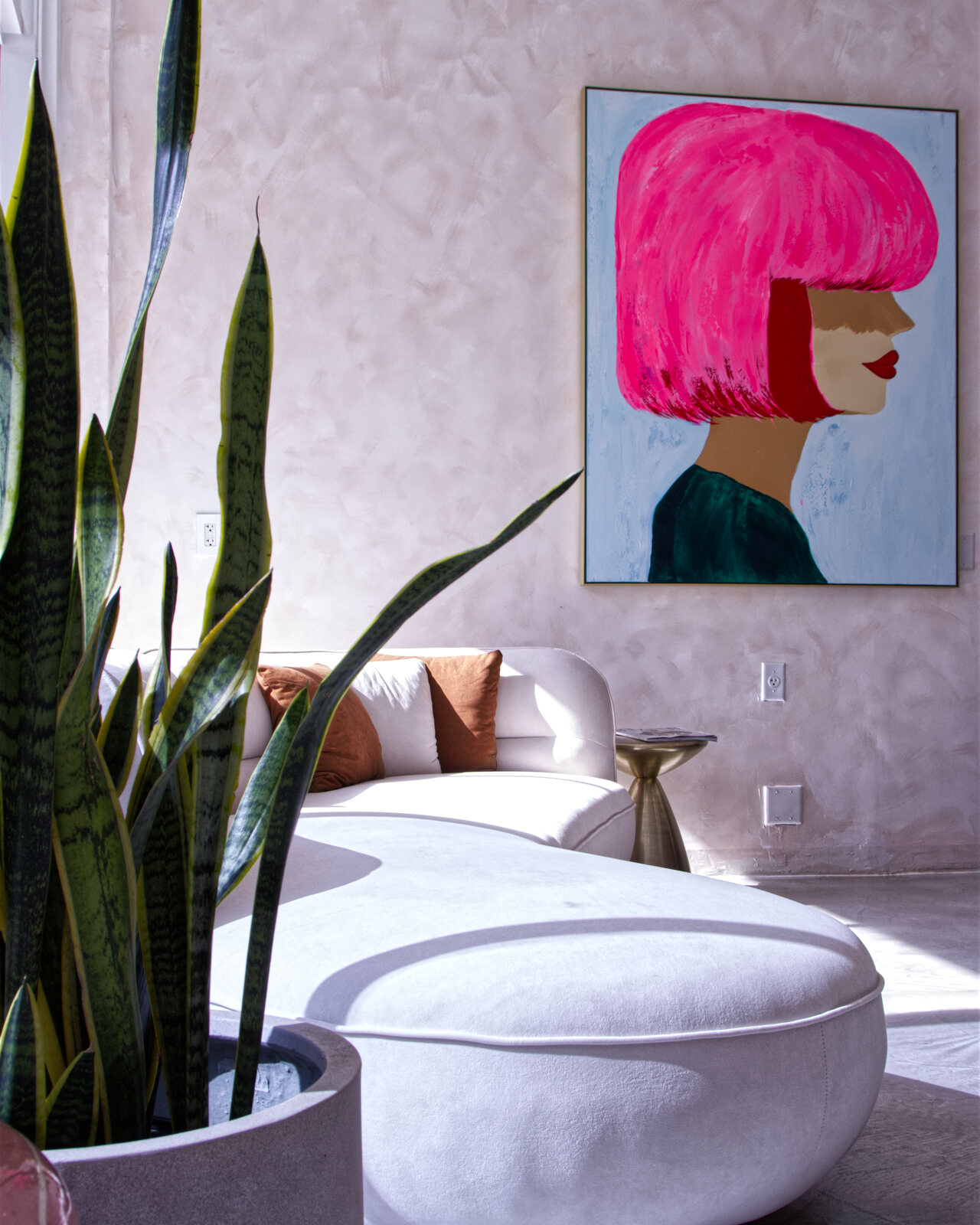 Red Market & Martial Vivot lounge — pink-plaster walls, curved white settee, pop-art portrait, snake plant