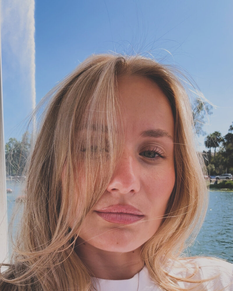 Long blonde hair with face-framing layers, photographed against outdoor blue sky and water